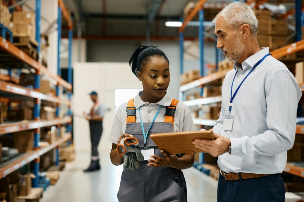 Mature foreman and black female worker using touchpad at distribution warehouse.