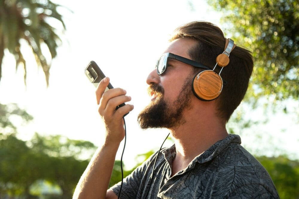 Side view of caucasian male recording voice message using mobile phone outdoors.