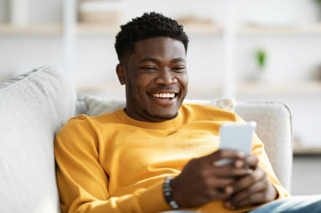 Smiling african american man reclining on couch with cellphone