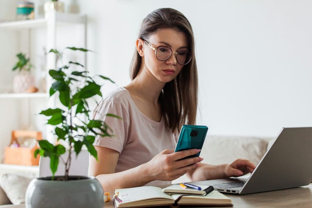 Young woman using mobile phone and laptop to work home, multiple devices